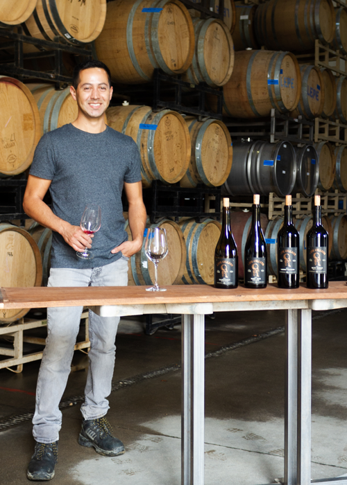 Miguel Lepe stands with his wine lineup in the barrel room at the winery.